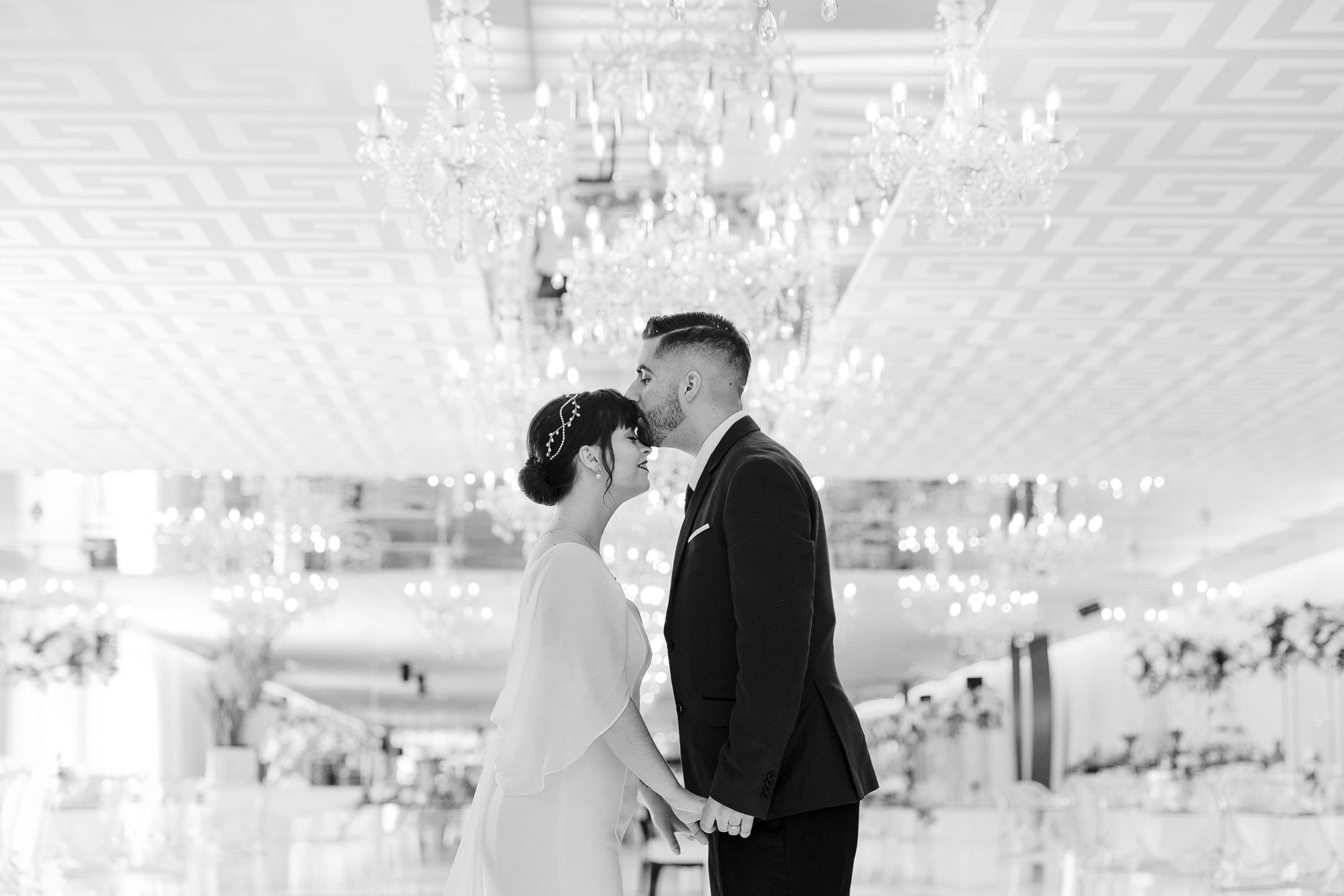 fotografia a preto e branco no salão da quinta dos pinheirais, com noivo a dar um beijo na testa da noiva. fotografo da feelin'motion
